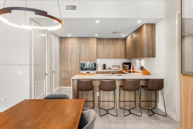 kitchen with pendant lighting, black microwave, sink, a kitchen bar, and kitchen peninsula