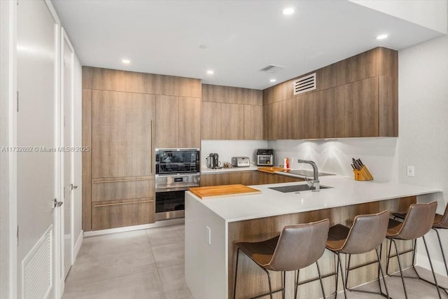 kitchen with sink, black microwave, a kitchen breakfast bar, kitchen peninsula, and oven