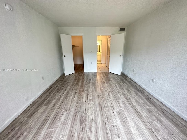 unfurnished bedroom featuring a spacious closet, light hardwood / wood-style floors, a closet, and a textured ceiling