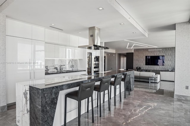 kitchen with white cabinetry, island range hood, a breakfast bar, and dark stone countertops