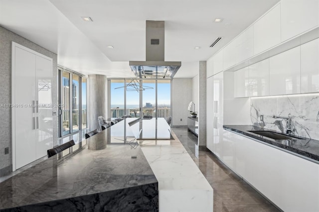 kitchen featuring sink, island range hood, white cabinets, and dark stone counters