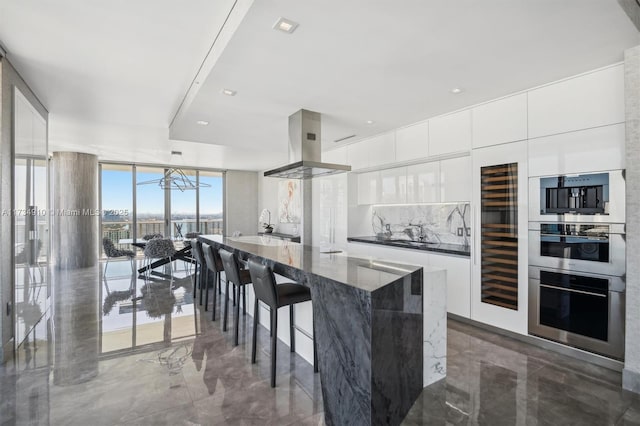 kitchen featuring a wall of windows, island range hood, a kitchen bar, and white cabinets