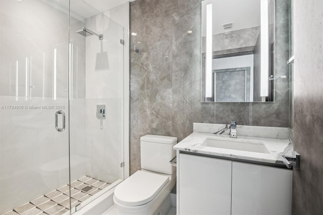 bathroom with vanity, toilet, a shower with door, and tile walls