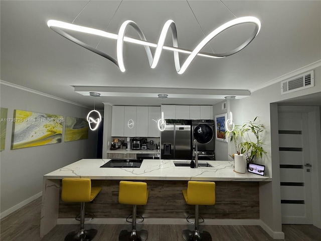 kitchen featuring stacked washer / drying machine, a breakfast bar, sink, white cabinets, and black appliances