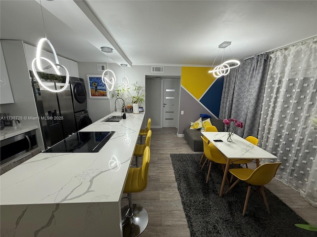 kitchen featuring stacked washer and dryer, sink, hanging light fixtures, black appliances, and light stone countertops