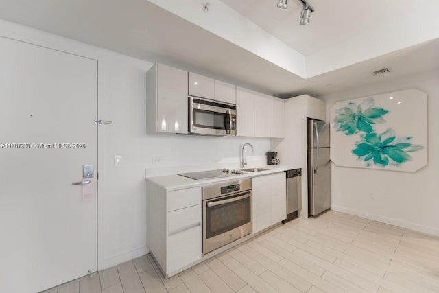 kitchen featuring sink, rail lighting, appliances with stainless steel finishes, white cabinets, and light wood-type flooring