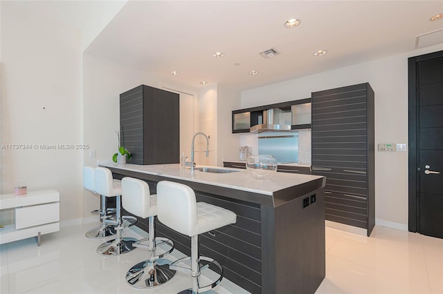 kitchen with sink, stove, a kitchen island with sink, light tile patterned floors, and wall chimney exhaust hood