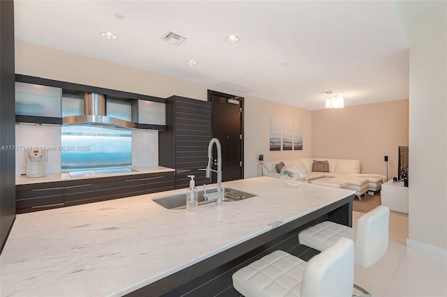 kitchen with black electric stovetop, a kitchen breakfast bar, sink, and wall chimney range hood