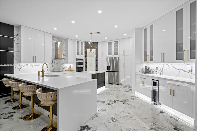 kitchen featuring wall chimney exhaust hood, sink, a breakfast bar area, appliances with stainless steel finishes, and white cabinets