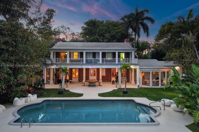 back house at dusk with a balcony, an outdoor fire pit, and a patio