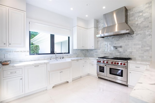 kitchen featuring sink, white cabinetry, backsplash, wall chimney exhaust hood, and range with two ovens