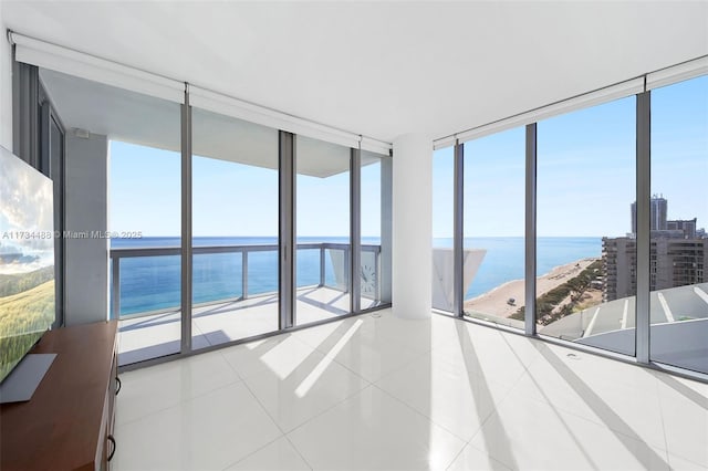 tiled empty room featuring a view of the beach, expansive windows, and a water view