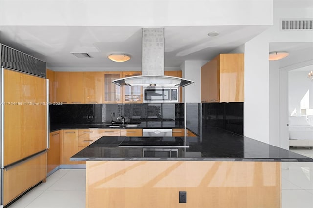 kitchen with sink, tasteful backsplash, island range hood, light tile patterned floors, and paneled refrigerator