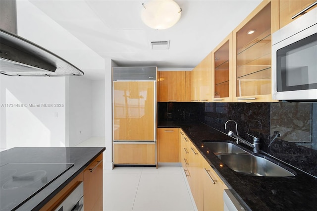 kitchen featuring black electric stovetop, a sink, stainless steel microwave, decorative backsplash, and paneled fridge