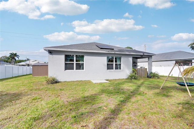 3425 SW Rosser Blvd, Port St Lucie, FL 34953 - rear view of house featuring roof with shingles, stucco siding, a fenced backyard, solar panels, and a lawn