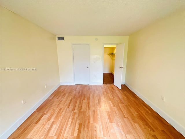 unfurnished bedroom featuring a closet, a walk in closet, and light hardwood / wood-style flooring