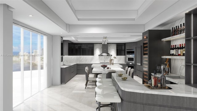 kitchen with wall chimney range hood, sink, a kitchen breakfast bar, a tray ceiling, and kitchen peninsula