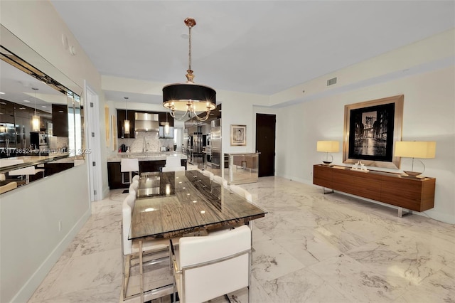 kitchen featuring a kitchen island, pendant lighting, backsplash, a chandelier, and wall chimney range hood