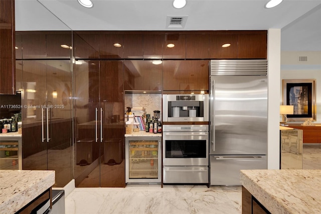 kitchen with dark brown cabinetry, appliances with stainless steel finishes, and light stone countertops