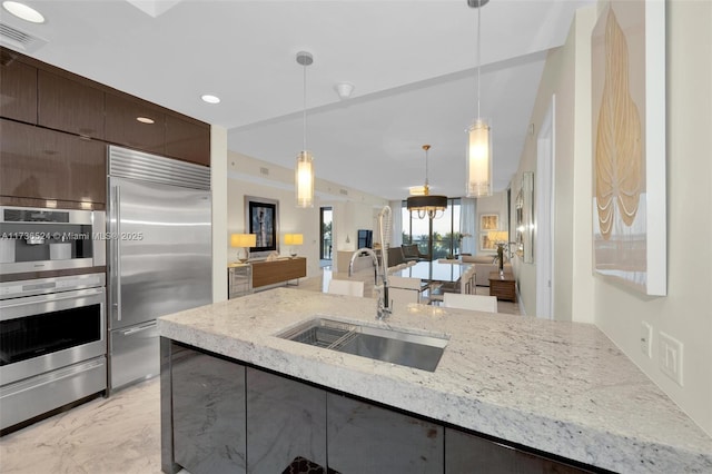 kitchen with appliances with stainless steel finishes, sink, pendant lighting, and dark brown cabinets