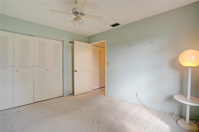 unfurnished bedroom with ceiling fan, two closets, light colored carpet, and a textured ceiling