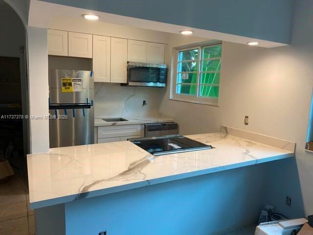 359 Meridian Ave Unit A207, Miami Beach, FL 33139 - kitchen featuring appliances with stainless steel finishes, a peninsula, white cabinets, light stone countertops, and arched walkways