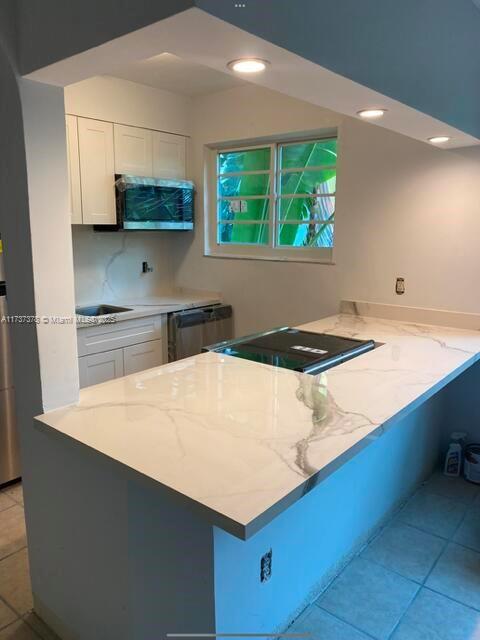 359 Meridian Ave Unit A207, Miami Beach, FL 33139 - kitchen with white cabinets, a peninsula, light stone counters, light tile patterned floors, and stainless steel dishwasher