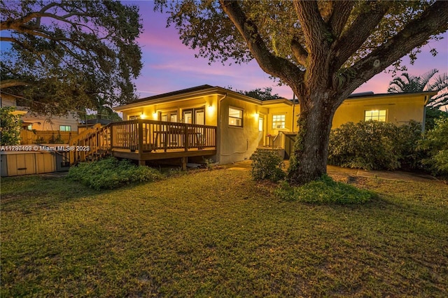 back house at dusk with a hot tub, a deck, and a lawn