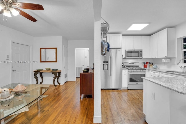 kitchen featuring appliances with stainless steel finishes, sink, white cabinets, light stone countertops, and light hardwood / wood-style flooring