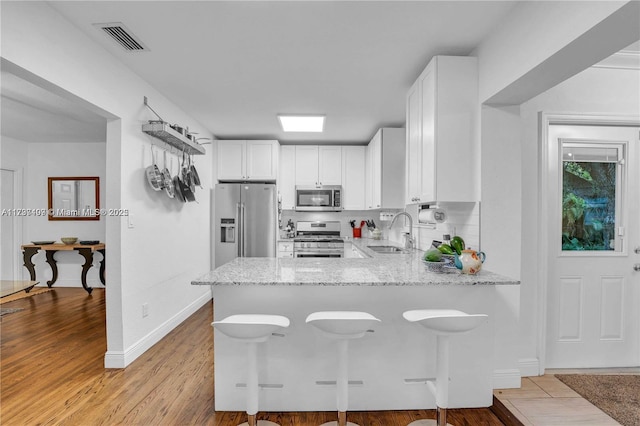 kitchen with sink, white cabinets, light stone counters, kitchen peninsula, and stainless steel appliances