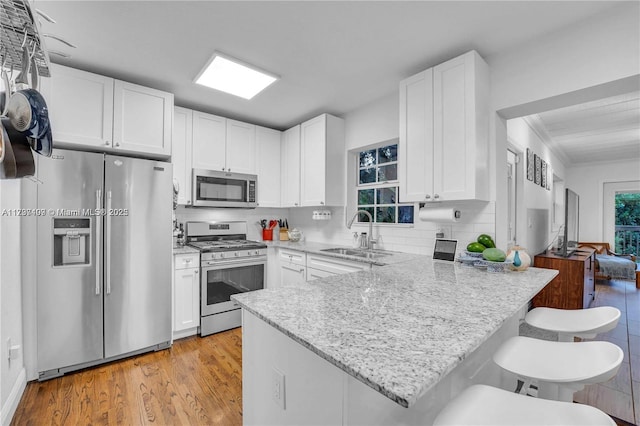 kitchen with appliances with stainless steel finishes, sink, white cabinets, a kitchen breakfast bar, and kitchen peninsula