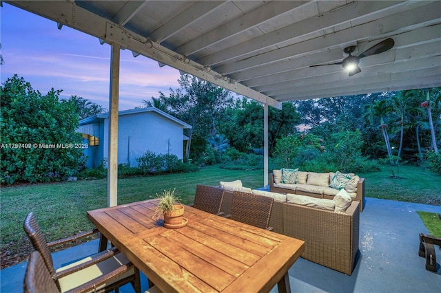 patio terrace at dusk featuring ceiling fan, outdoor lounge area, and a lawn