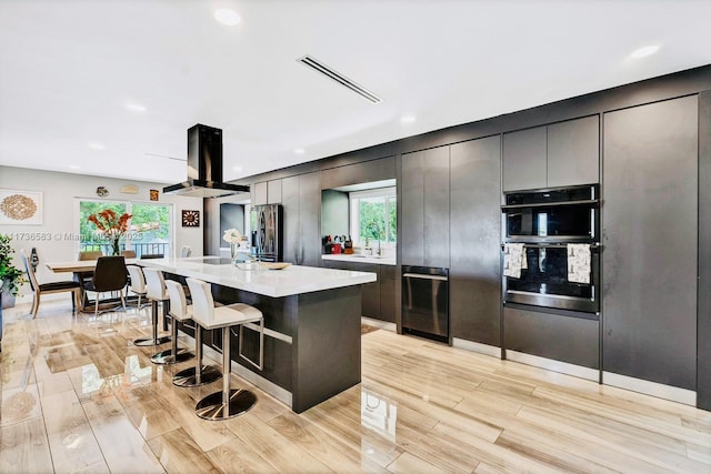 kitchen featuring visible vents, a breakfast bar, island exhaust hood, light countertops, and stainless steel refrigerator with ice dispenser