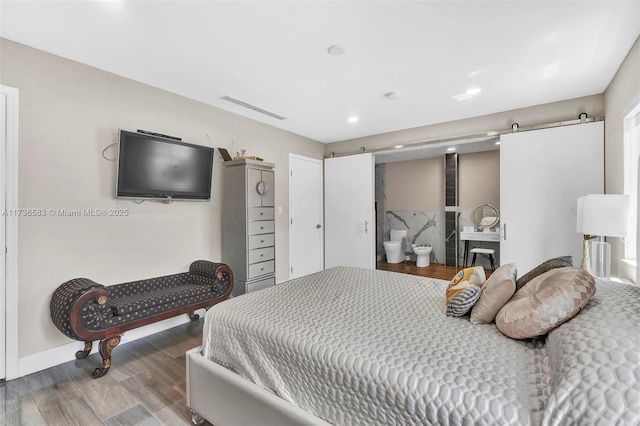 bedroom with a barn door, visible vents, and wood finished floors