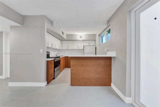 kitchen featuring baseboards, stainless steel electric range oven, light countertops, freestanding refrigerator, and white cabinetry