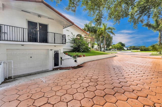 view of side of home with stucco siding, a balcony, and an attached garage