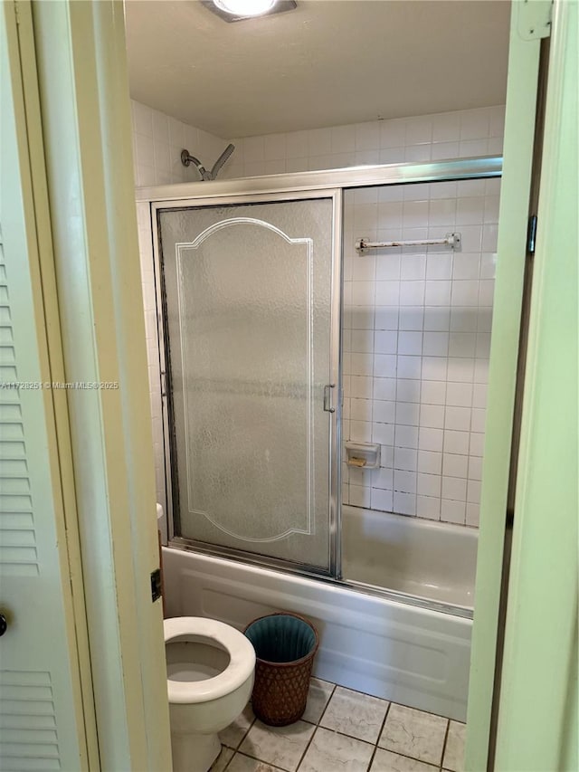 bathroom featuring tile patterned flooring, bath / shower combo with glass door, and toilet