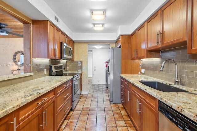 kitchen with light stone counters, stainless steel appliances, sink, and backsplash