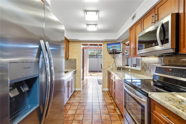 kitchen with stainless steel appliances, tasteful backsplash, light stone countertops, and light tile patterned floors