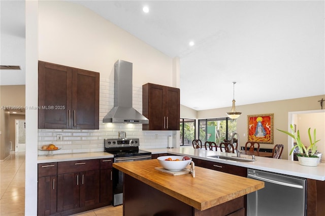 kitchen featuring wall chimney exhaust hood, sink, butcher block countertops, kitchen peninsula, and stainless steel appliances