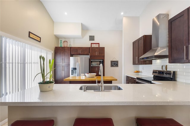 kitchen with wall chimney exhaust hood, a breakfast bar, sink, appliances with stainless steel finishes, and kitchen peninsula