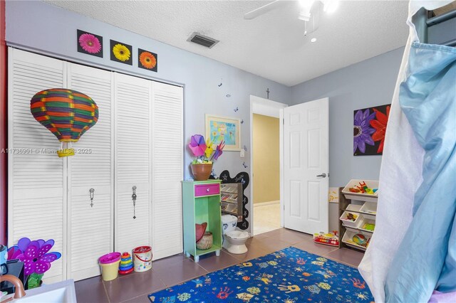 rec room featuring ceiling fan, a textured ceiling, and dark tile patterned floors