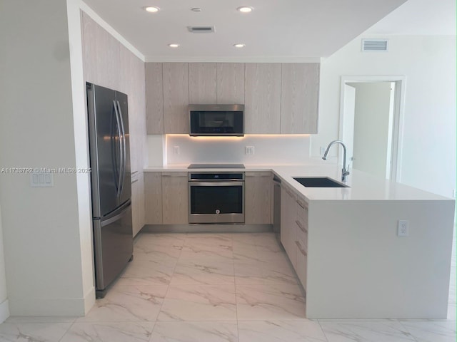 kitchen with appliances with stainless steel finishes, sink, light brown cabinets, and kitchen peninsula