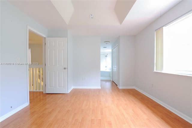 empty room with a tray ceiling and light hardwood / wood-style floors