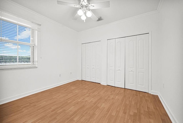 unfurnished bedroom with ceiling fan, crown molding, light hardwood / wood-style flooring, and multiple closets