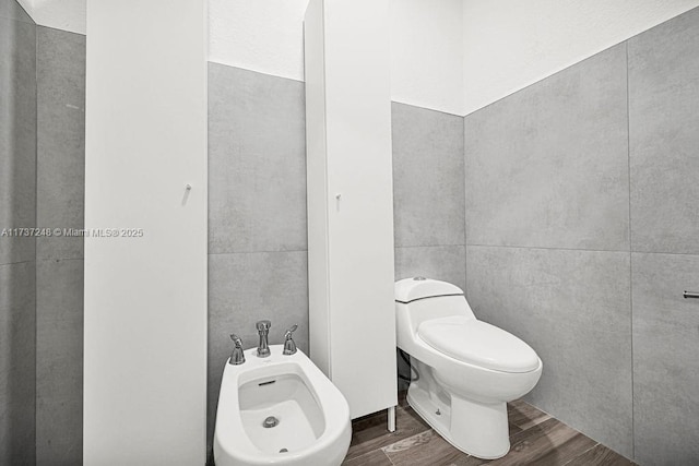 bathroom with a bidet, wood-type flooring, tile walls, and toilet