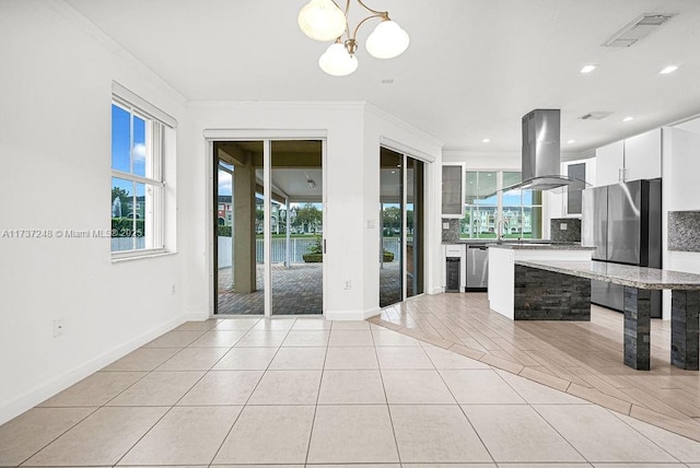 kitchen featuring a wealth of natural light, island range hood, white cabinets, and light tile patterned floors