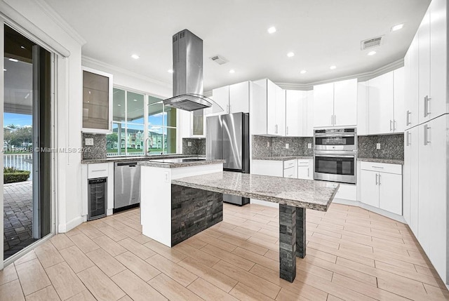 kitchen featuring dark stone countertops, white cabinets, island exhaust hood, a center island, and stainless steel appliances