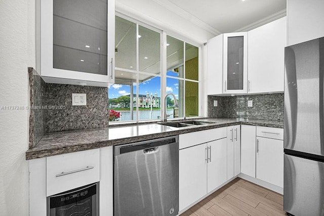 kitchen featuring sink, ornamental molding, stainless steel appliances, light hardwood / wood-style floors, and white cabinets