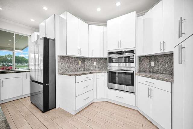 kitchen with white cabinetry, tasteful backsplash, dark stone countertops, and appliances with stainless steel finishes